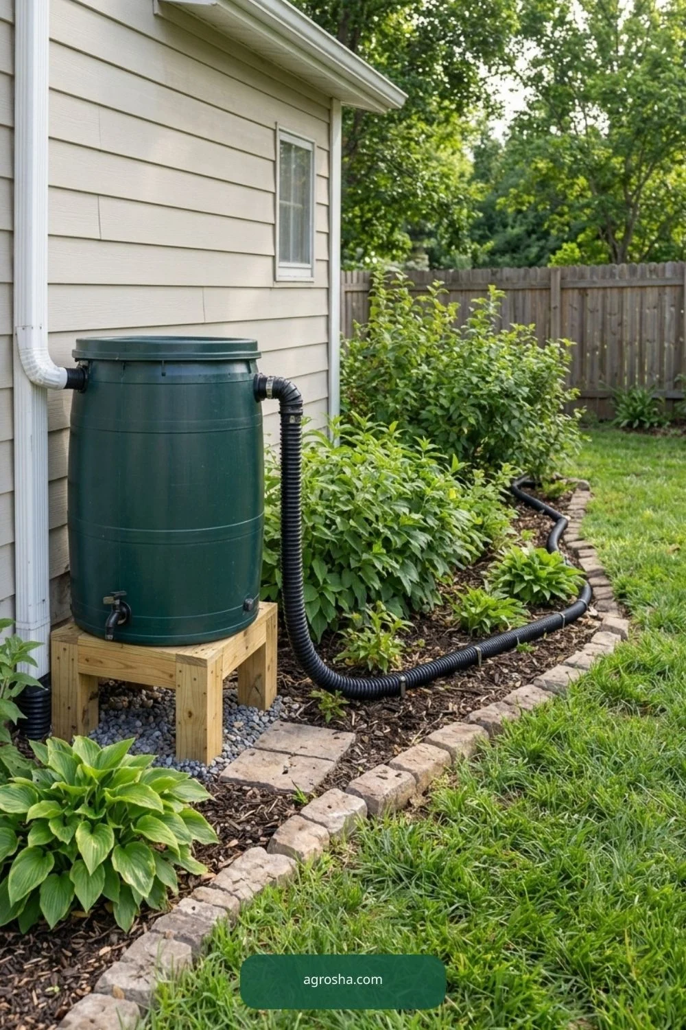 Installed black overflow hose running from elevated rain barrel through flowerbed toward drainage area