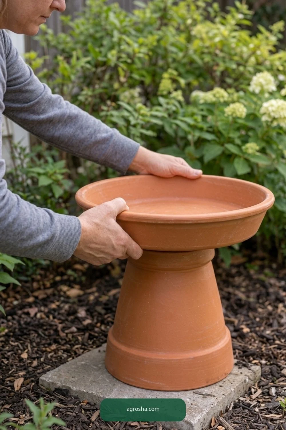 Hands lowering a shallow terracotta saucer onto an inverted pot support